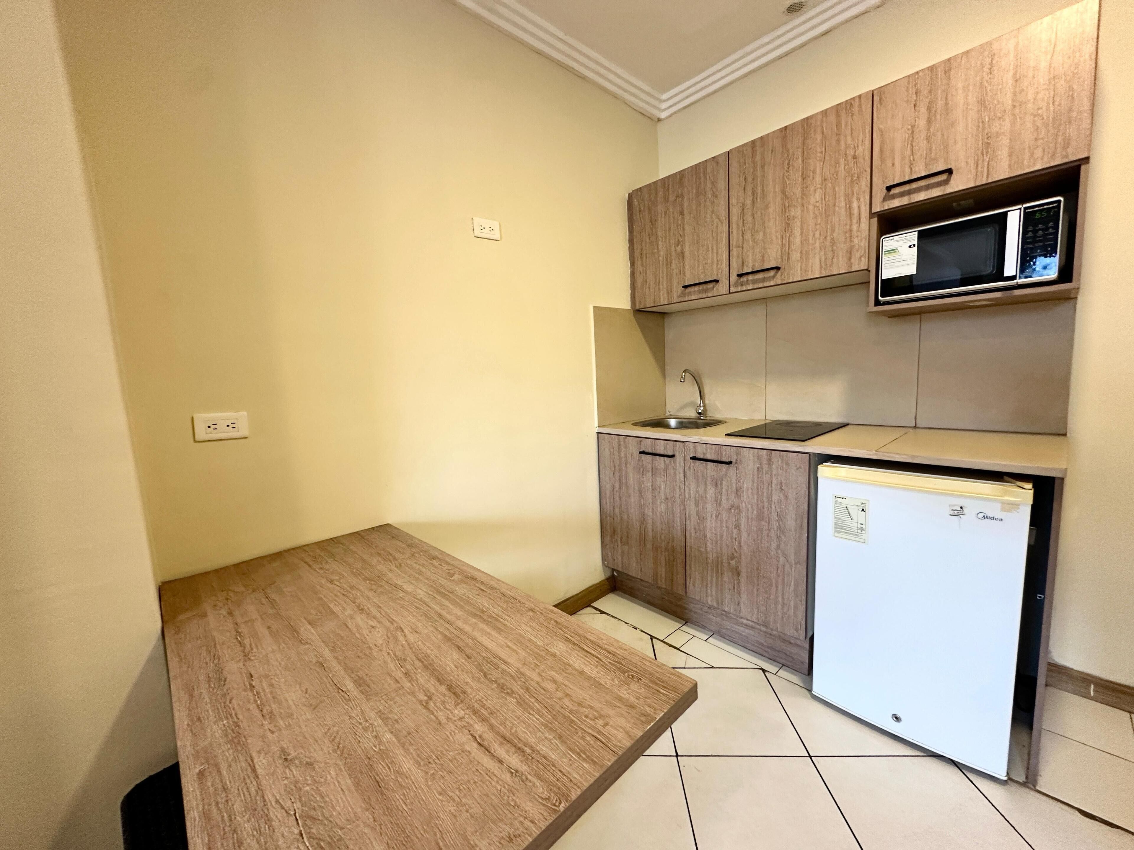 A small kitchen with wooden cabinets, a microwave, a sink, and a refrigerator.