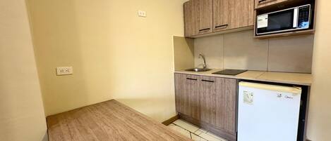 A small kitchen with wooden cabinets, a microwave, a sink, and a refrigerator.
