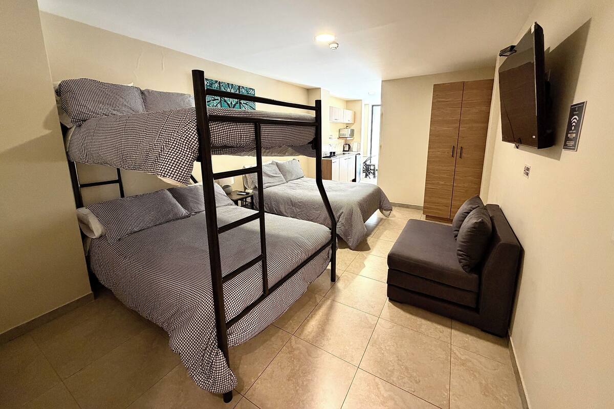 A room with bunk beds, a sofa, a TV, and a kitchenette.