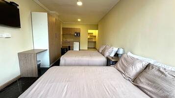 Quarto de hotel com duas camas, cozinha compacta, micro-ondas e televisão na parede.