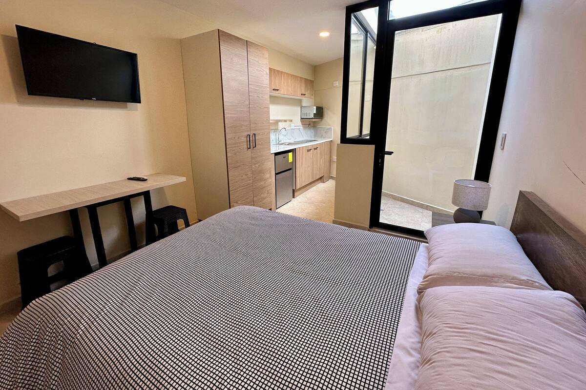 A bedroom with a bed, a desk, a TV, and a sliding door to a balcony.