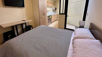 A bedroom with a bed, a desk, a TV, and a sliding door to a balcony.