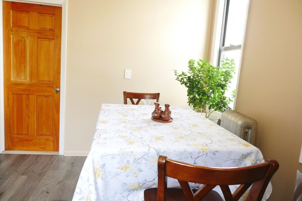 A dining area with a table set for two, a wooden door, a plant, and a window.