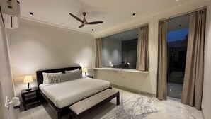 A bedroom with a bed, a nightstand, a lamp, a ceiling fan, a window with curtains, and a marble floor. - Guldaar - A Luxury Forest Retreat (Rajgarh)