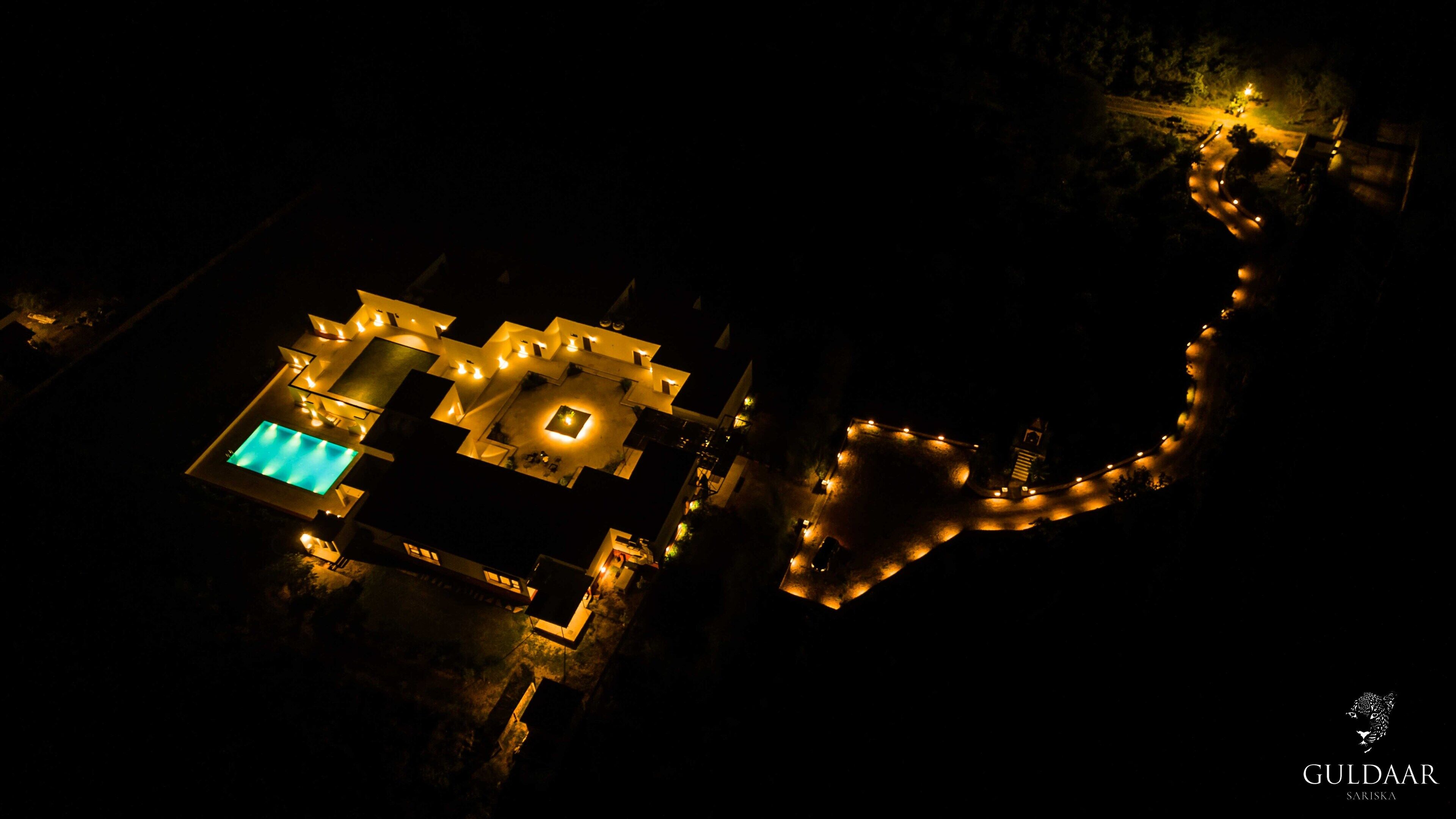 An aerial view of a modern resort with a pool, multiple buildings, and a well-lit pathway.