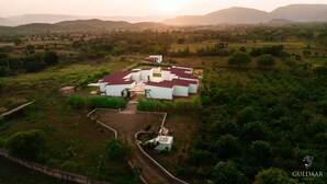 A rural property with multiple white buildings, a central courtyard, and surrounding greenery. - Guldaar - A Luxury Forest Retreat (Rajgarh)