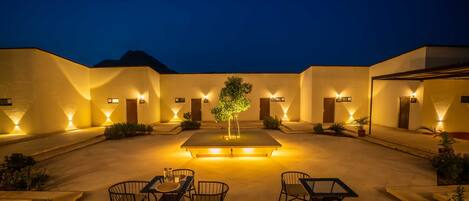 A courtyard with outdoor seating, a central table, and illuminated walls.