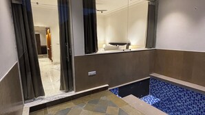 A hotel room with a checkered floor, a small pool with blue tiles, a ceiling fan, and a large mirror reflecting the room. - Guldaar - A Luxury Forest Retreat (Rajgarh)