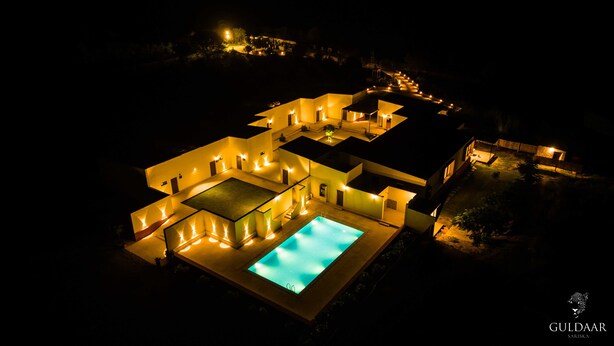 A modern hotel with a swimming pool, multiple connected buildings, and outdoor lighting. - Guldaar - A Luxury Forest Retreat (Rajgarh)