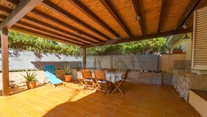 Eine überdachte Terrasse mit Fliesenboden, Holzmöbeln und Blumentöpfen.