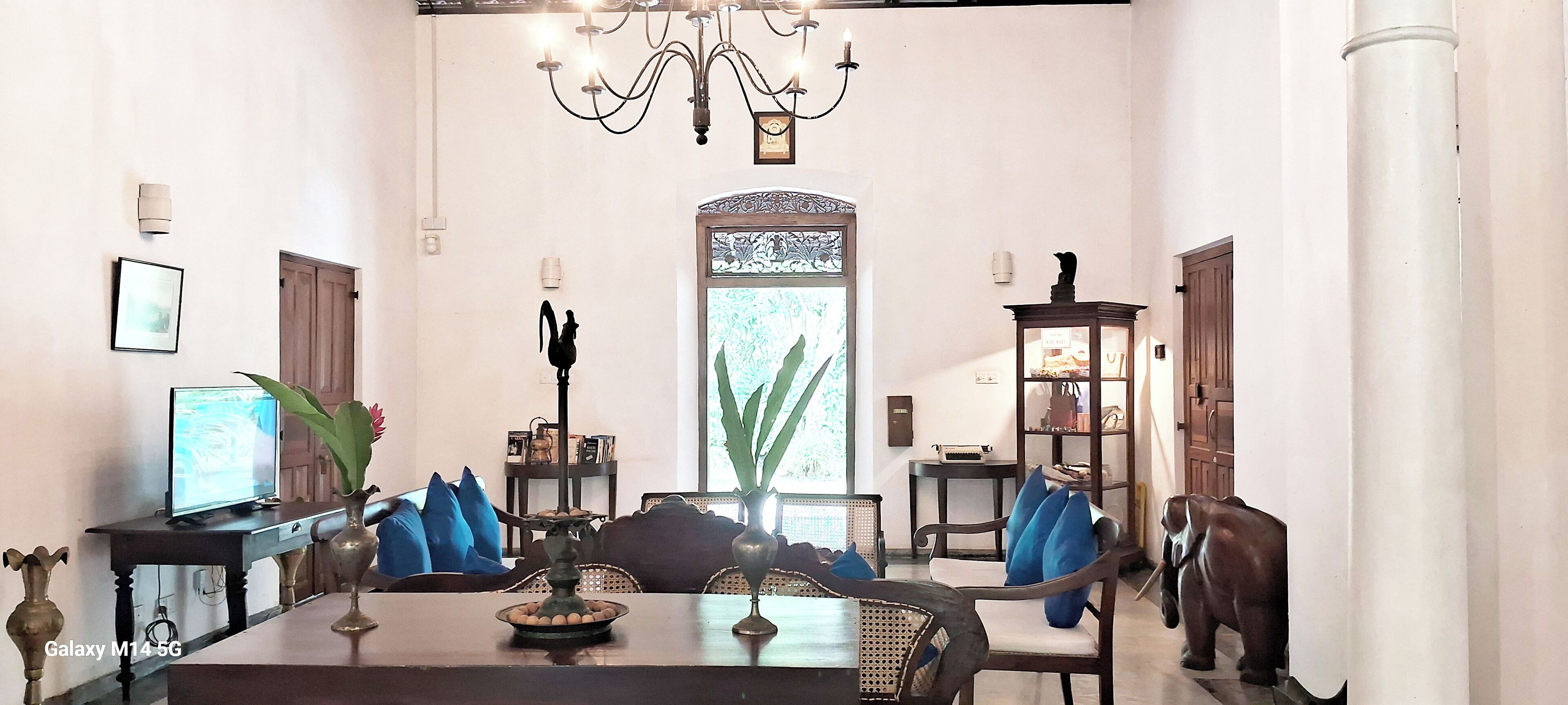 Un salón luminoso con una araña, una mesa de comedor con cojines azules, un televisor y una estantería.