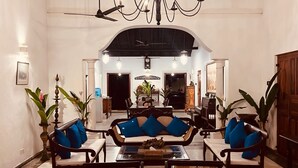 Une pièce spacieuse avec un plafond haut, un lustre et un coin salon comprenant un canapé et des fauteuils.