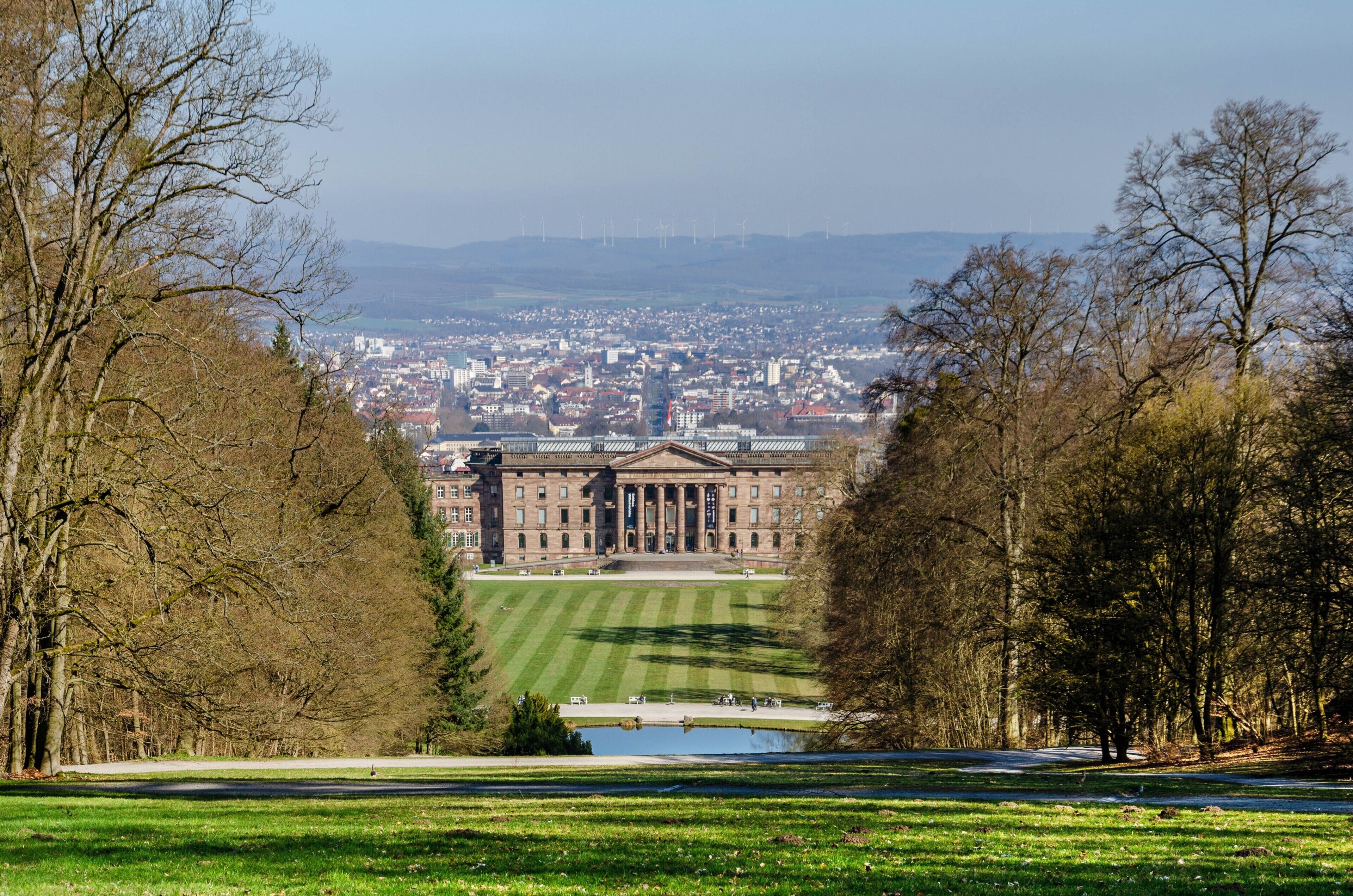 Ein großes Gebäude mit einem zentralen Innenhof, umgeben von Bäumen und Blick auf eine Stadtlandschaft.