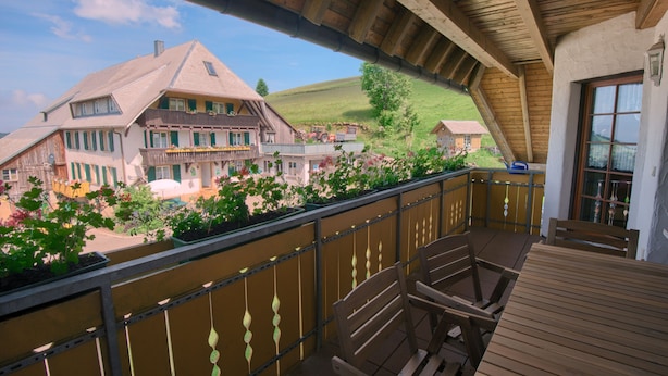 Un balcón con mobiliario de madera, vistas a casas y un paisaje verde.
