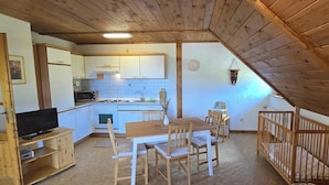 Cocina pequeña con armarios blancos, microondas y pileta. Hay una mesa de comedor con sillas y una cuna de madera.