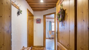 Un pasillo interior de madera con un banco, perchero y una puerta que da a una habitación con una silla y un ventanal.