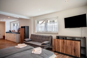 Une chambre d’hôtel moderne équipée d’un canapé, de deux lits, d’une télévision et d’une kitchenette.