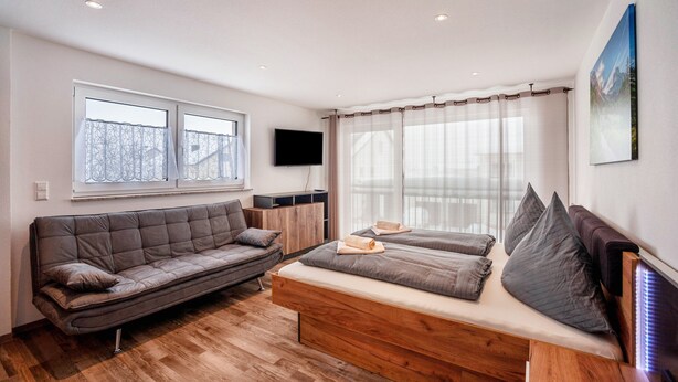 A modern room with a sofa, a bed, a TV, and a window with curtains. - Studio Apartment 'Ferienwohnung Legau' with Wi-Fi (Legau)