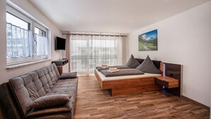 A modern living room with a sofa, a bed with storage, a TV, and a painting on the wall. - Studio Apartment 'Ferienwohnung Legau' with Wi-Fi (Legau)