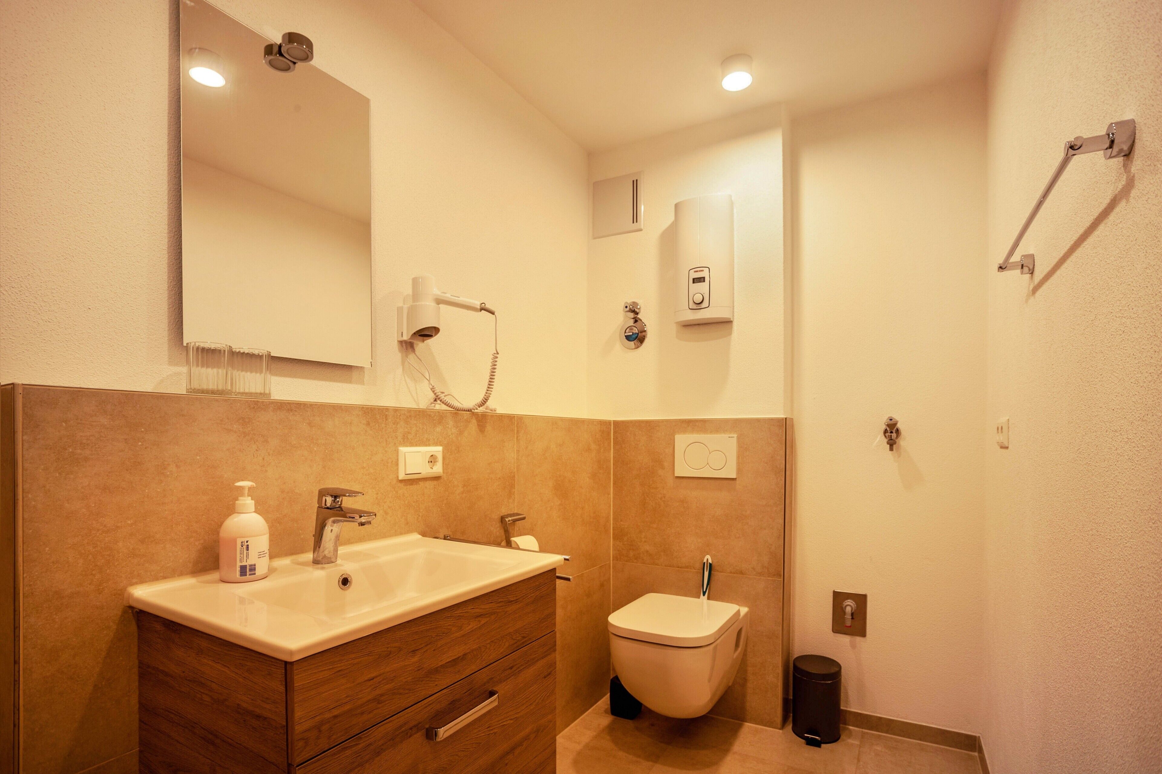 A bathroom with a sink, vanity, mirror, toilet, and towel rack.