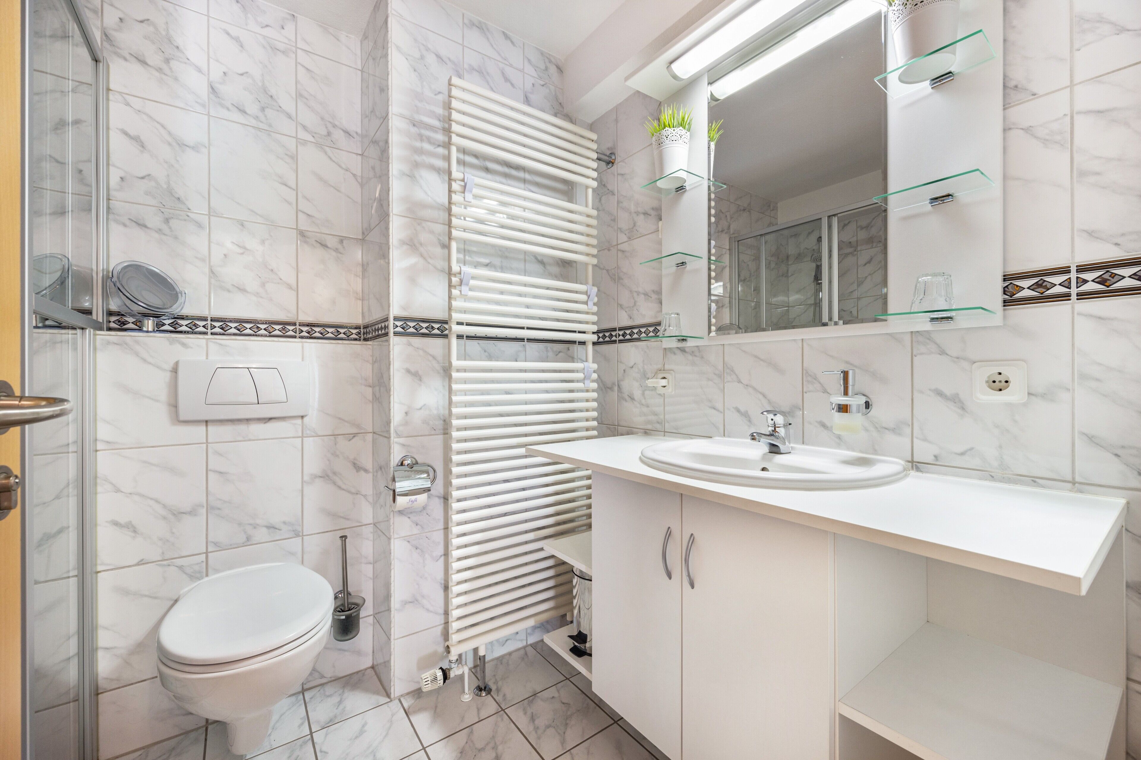 Ein Badezimmer mit Toilette, Waschbecken, einer Duschkabine aus Glas, einem Handtuchhalter und einem Spiegel.