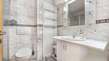 Ein Badezimmer mit Toilette, Waschbecken, einer Duschkabine aus Glas, einem Handtuchhalter und einem Spiegel.