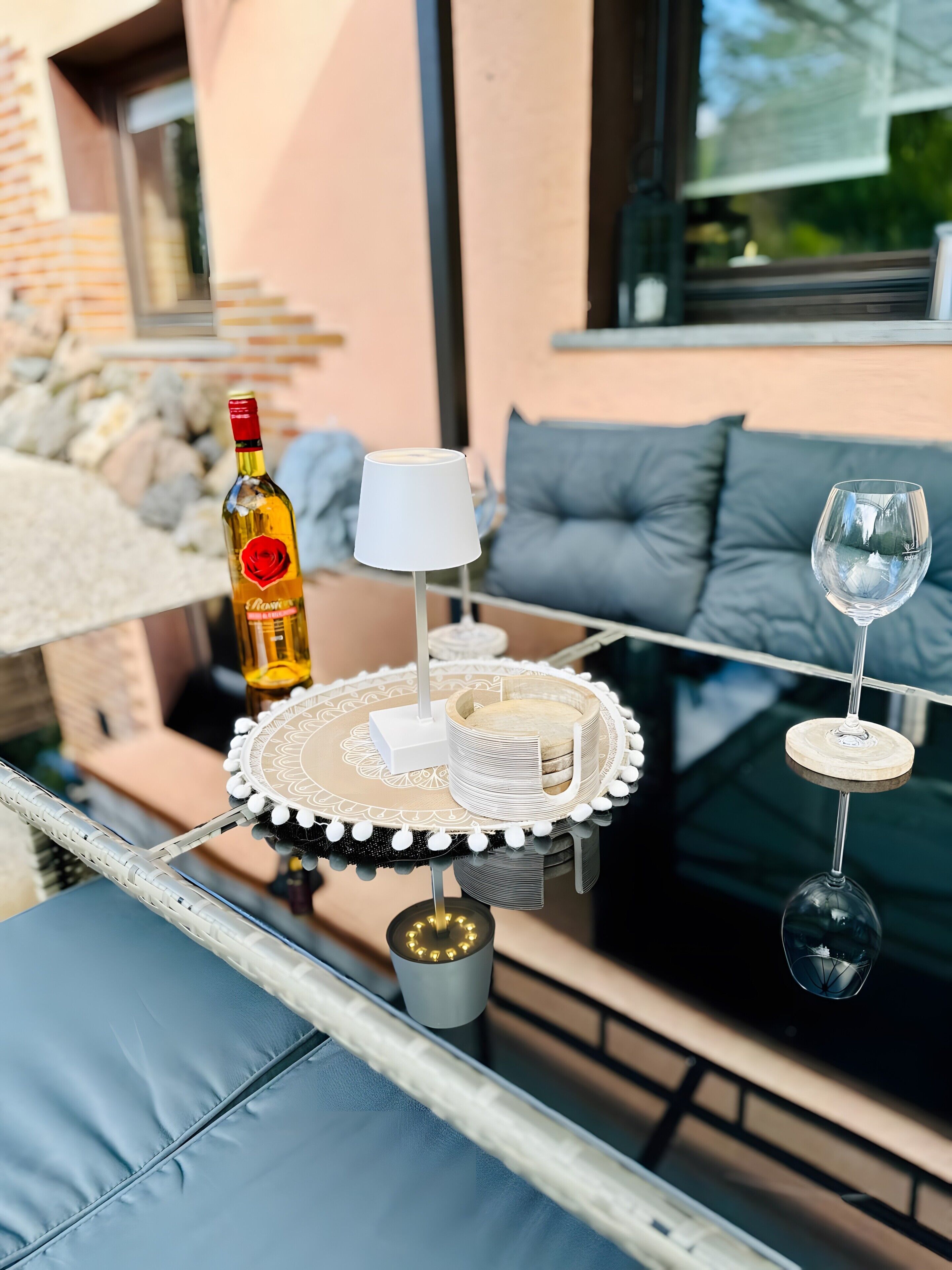 Uma mesa com uma garrafa, uma luminária, suportes para copos e um copo.