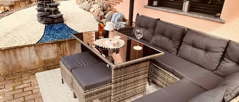 A covered patio area with a seating arrangement, a small water feature, and a view of the surrounding landscape.