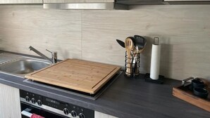A modern kitchen with a wooden cutting board, stainless steel sink, and a stove. - Apartment 'Bella Petit' with Private Terrace and Wi-Fi (Büdingen (Wolferborn))