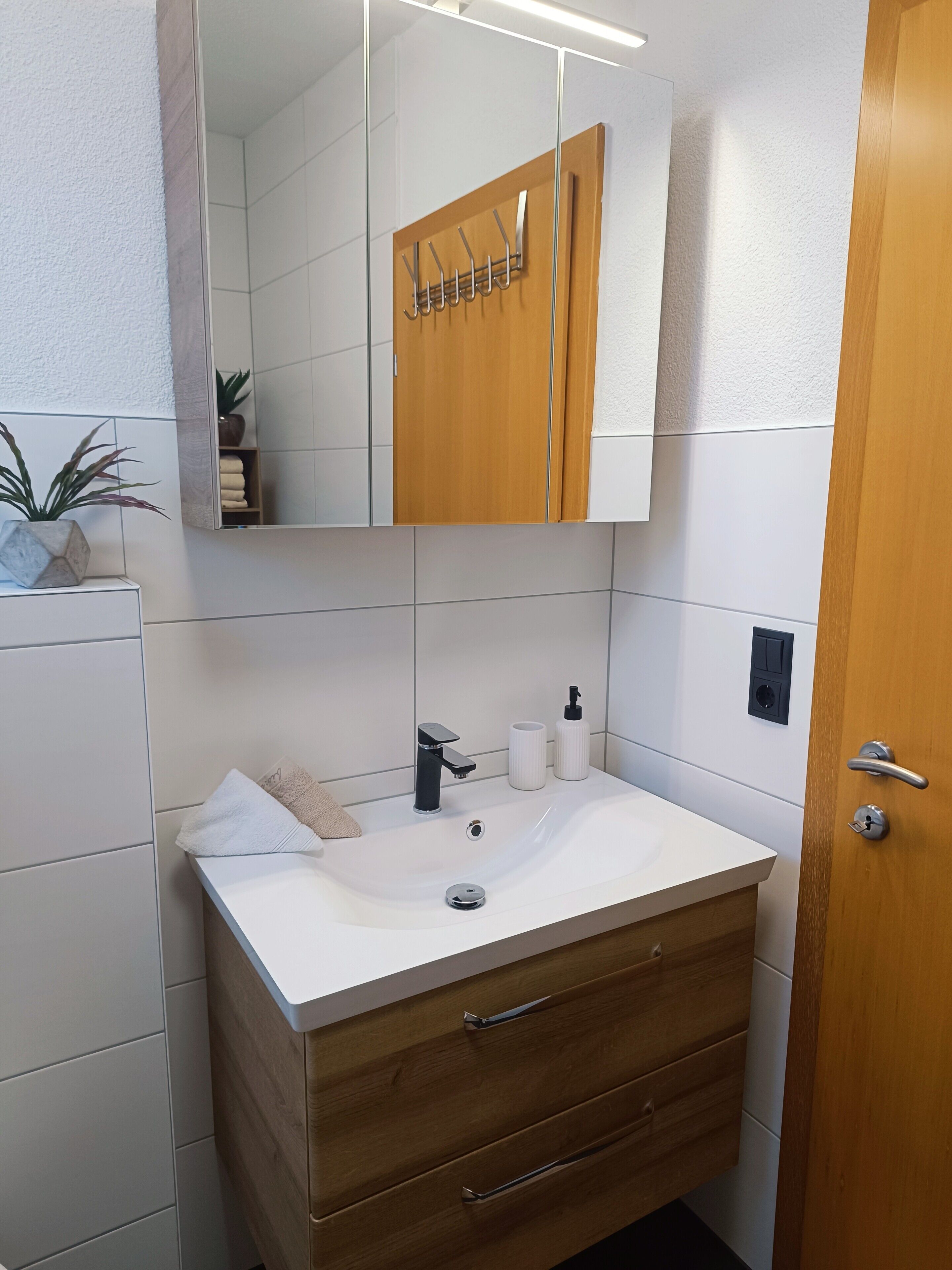 Une salle de bain avec un lavabo blanc, un meuble-lavabo en bois, un miroir et un porte-serviettes.