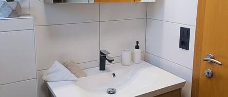 Une salle de bain avec un lavabo blanc, un meuble-lavabo en bois, un miroir et un porte-serviettes.