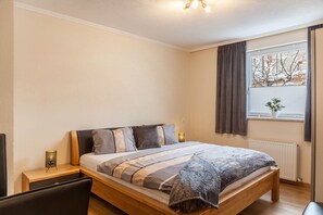 Una camera da letto con un letto, comodini, una finestra con tende, un termosifone e una pianta sul davanzale.