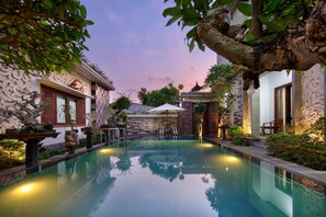 Ein ruhiger Poolbereich mit klarem Wasser, Zierpflanzen und traditioneller Architektur.