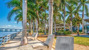 Un paseo marítimo con palmeras, bancos y una zona de estar cubierta.