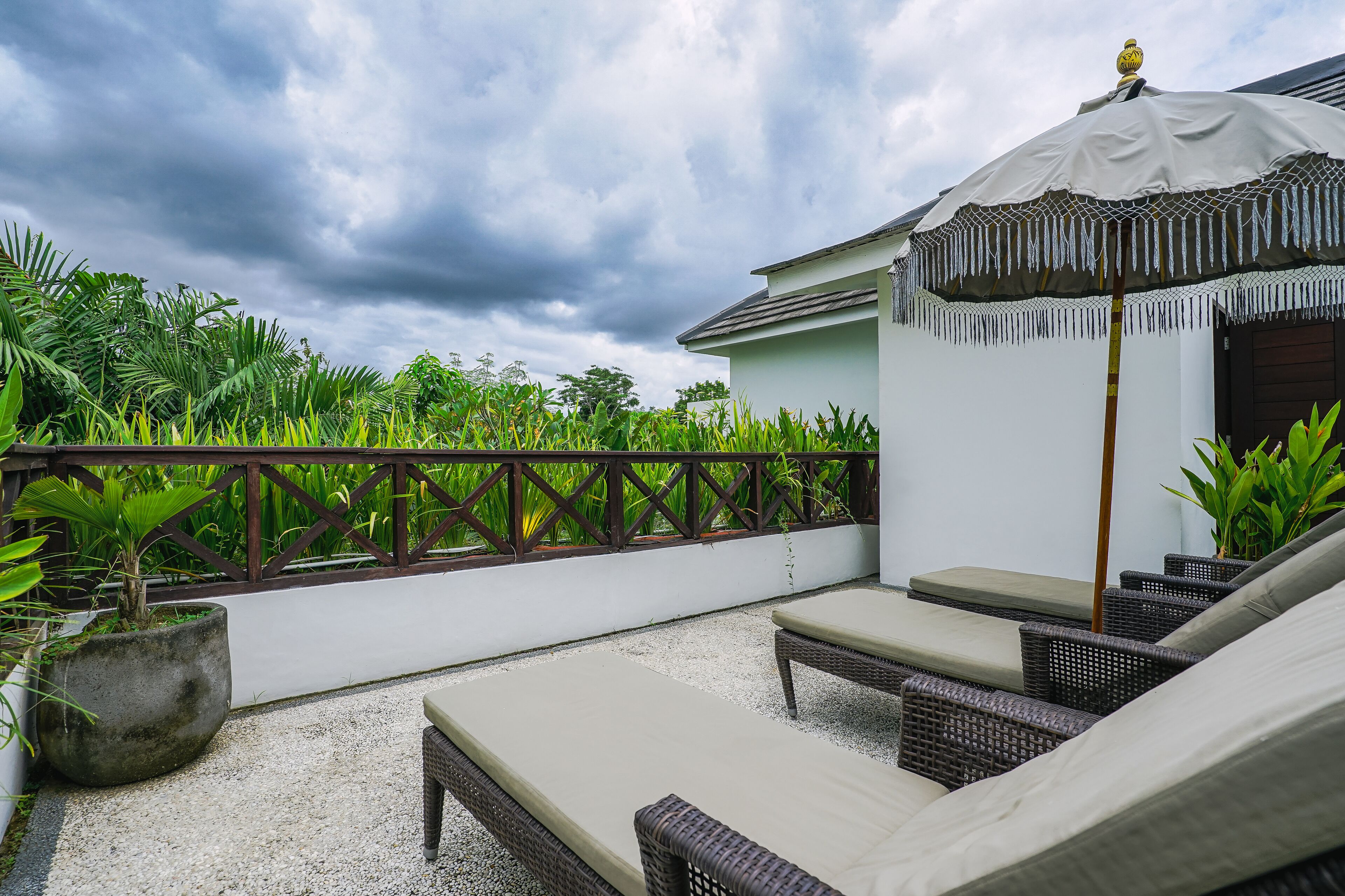 A rooftop terrace with wicker lounge chairs, a large umbrella, and lush greenery in the background.