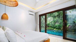 Ein Schlafzimmer mit Bett, Deckenventilator, Klimaanlage und Blick auf einen Swimmingpool und Grünflächen.
