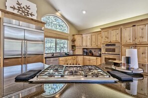 A modern kitchen with a central island, stainless steel appliances, wooden cabinets, and a large window. - National Forest & River | Hot Tub | Game Room (South Lake Tahoe)