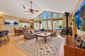 A spacious living room with a fireplace, large windows, and a dining area. - Ski Basecamp, Forest Land, Hot Tub & Pool Table (South Lake Tahoe)