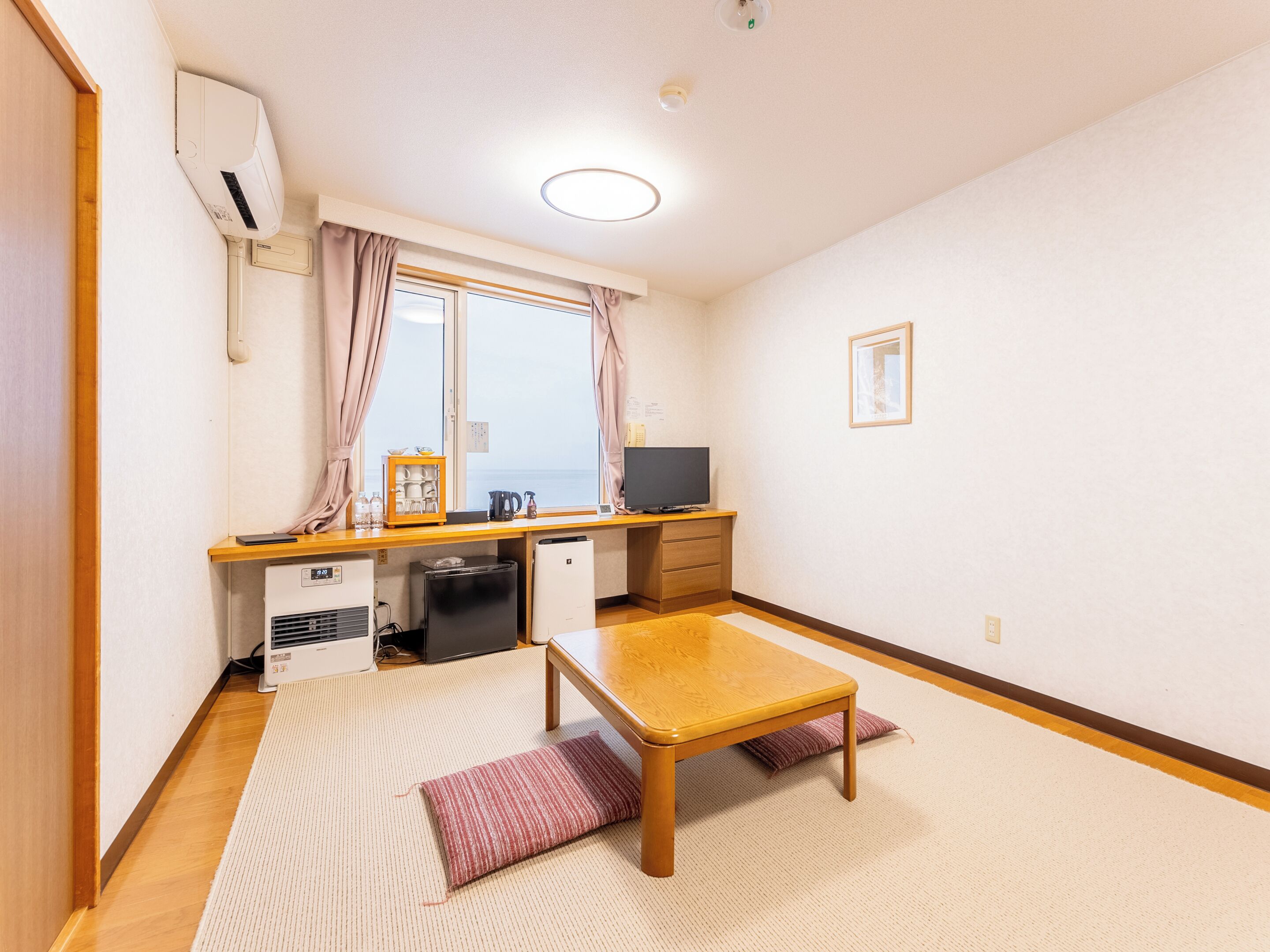 Habitación compacta con kitchenette, una mesita, sofá y ventana con cortinas.