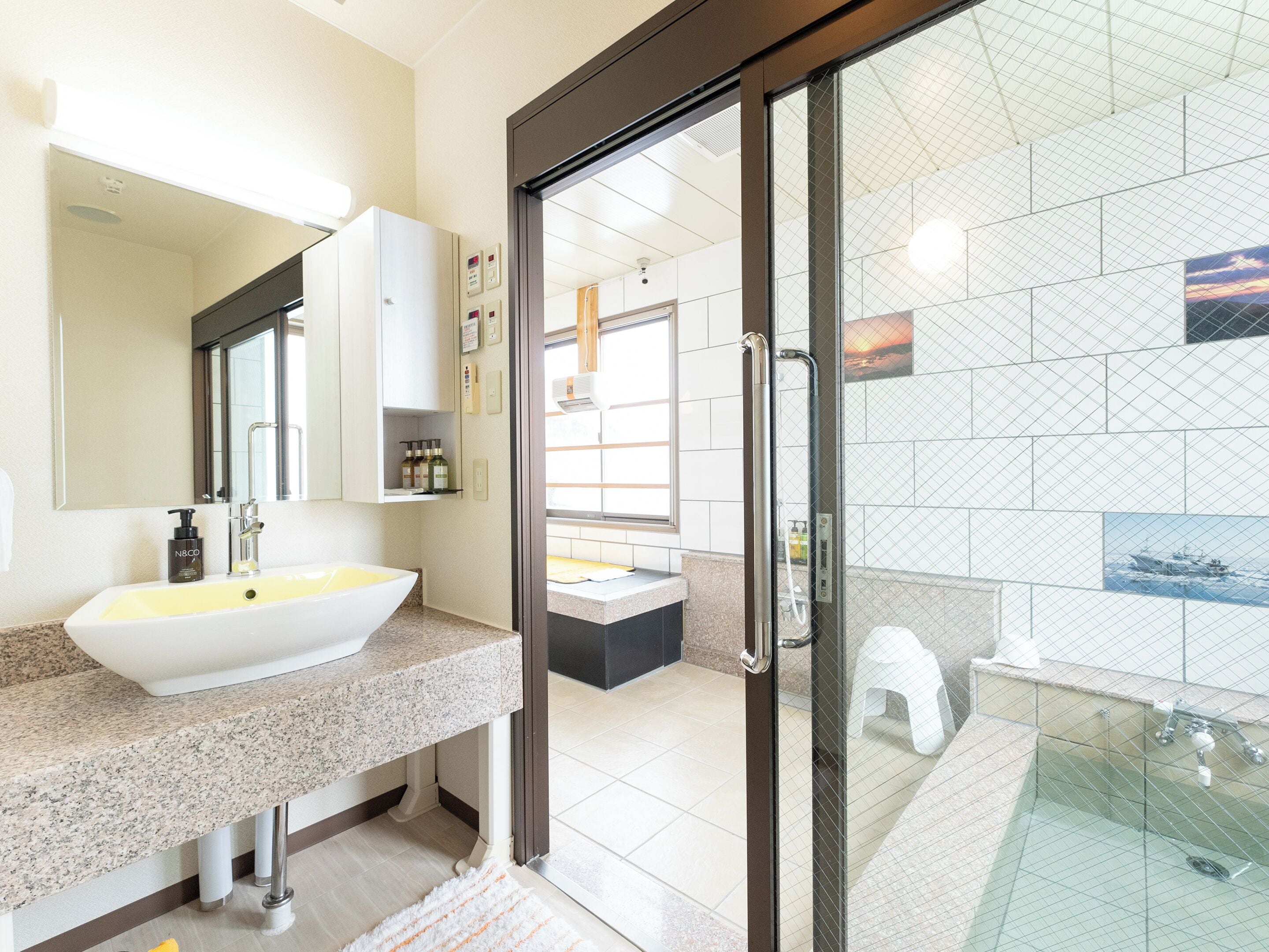 A modern bathroom with a large white sink, a glass shower enclosure, and a view of the adjacent bedroom.