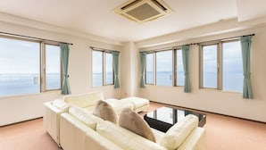 A spacious living room with a large sofa, a coffee table, and a view of the sea through multiple windows. - Livemax Resort Shiretoko Seafront (Rausu)
