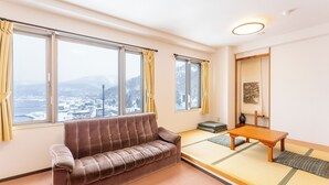 A room with a sofa, tatami flooring, a small table, and large windows with curtains. - Livemax Resort Shiretoko Seafront (Rausu)