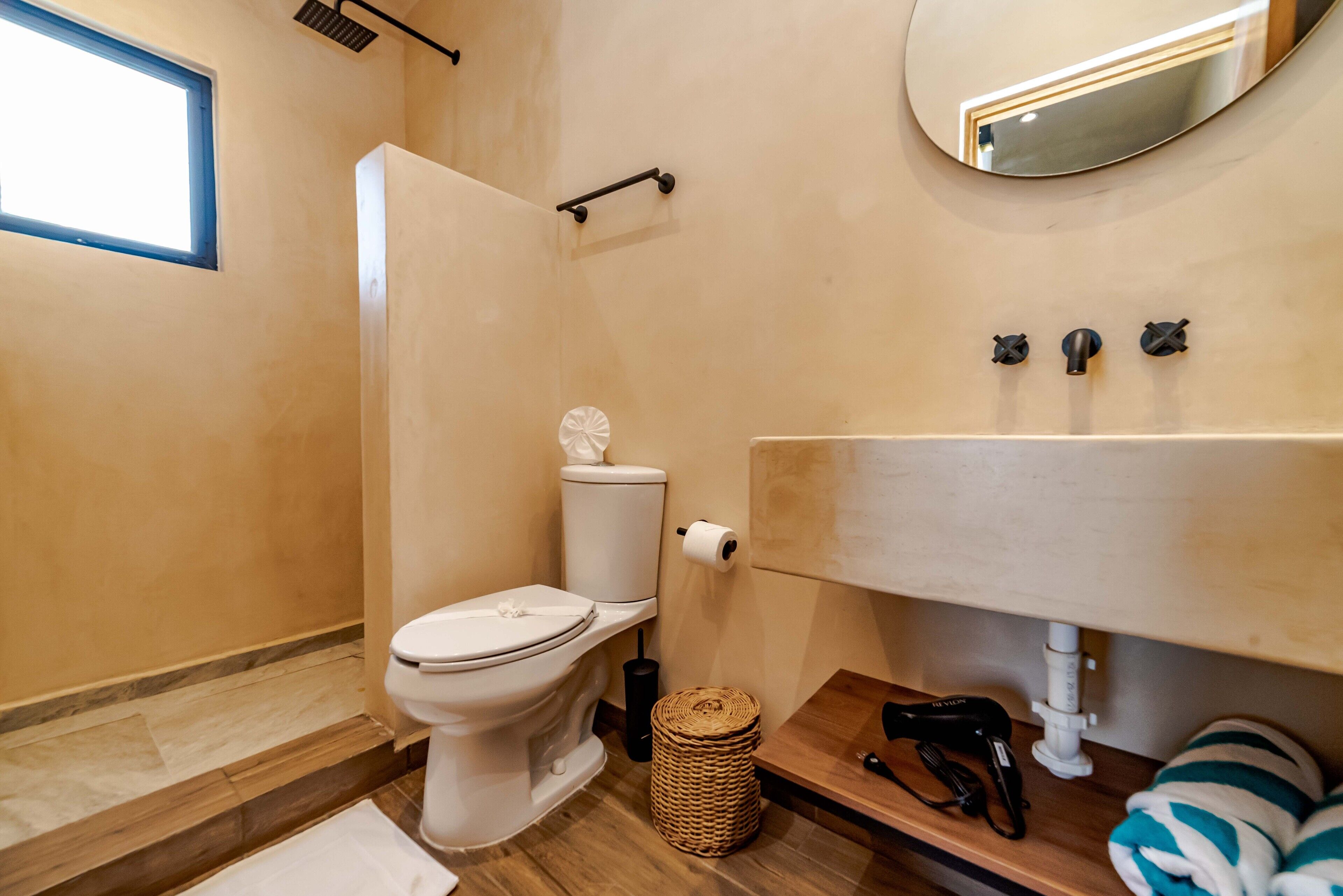 A bathroom with a toilet, a sink, a mirror, and a window.