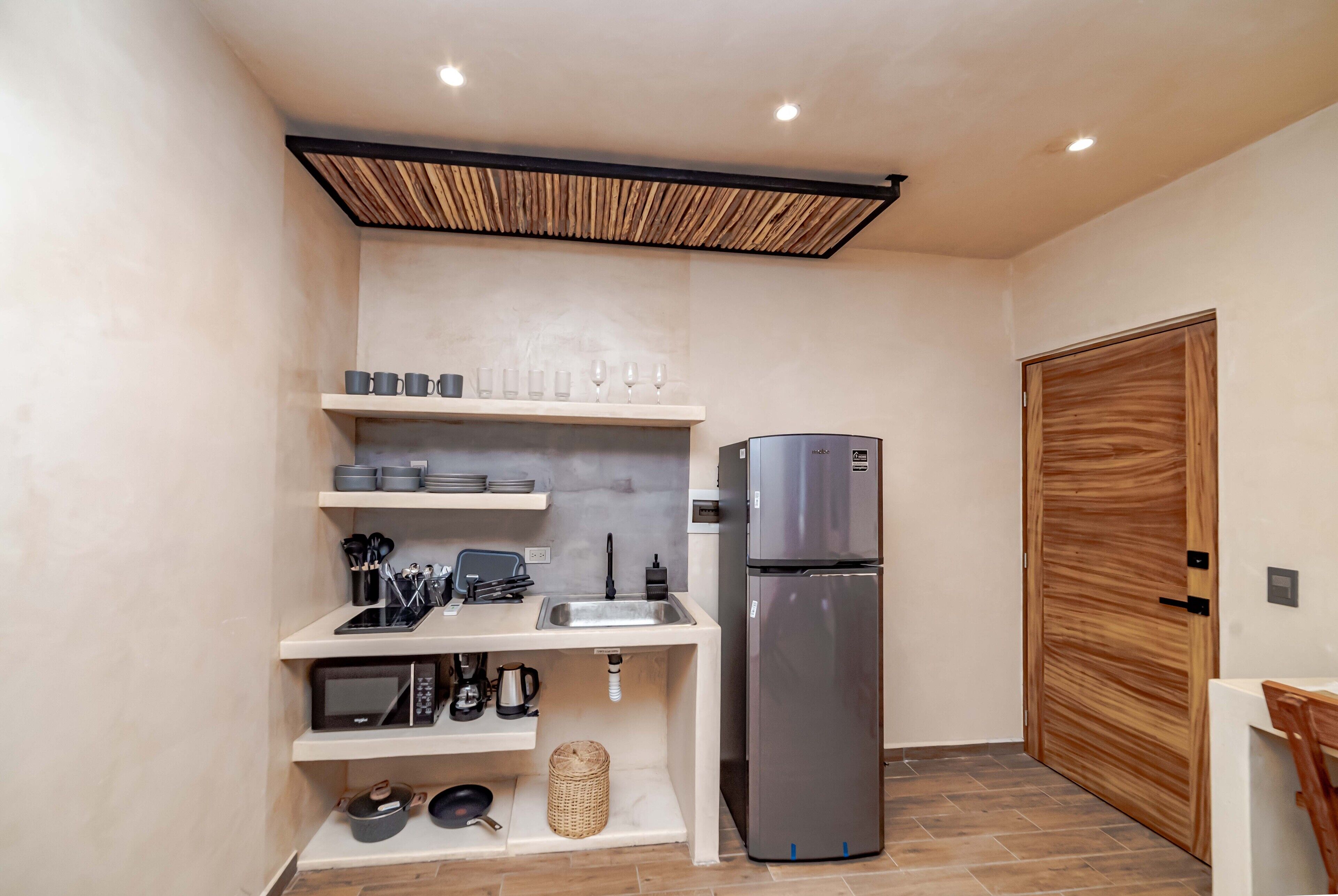 Una cucina compatta con un forno a microonde integrato, un frigorifero in acciaio inox e una porta in legno.