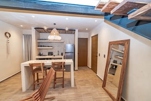 Una cocina moderna con una isla central, sillas de madera, una lámpara colgante y un refrigerador empotrado.