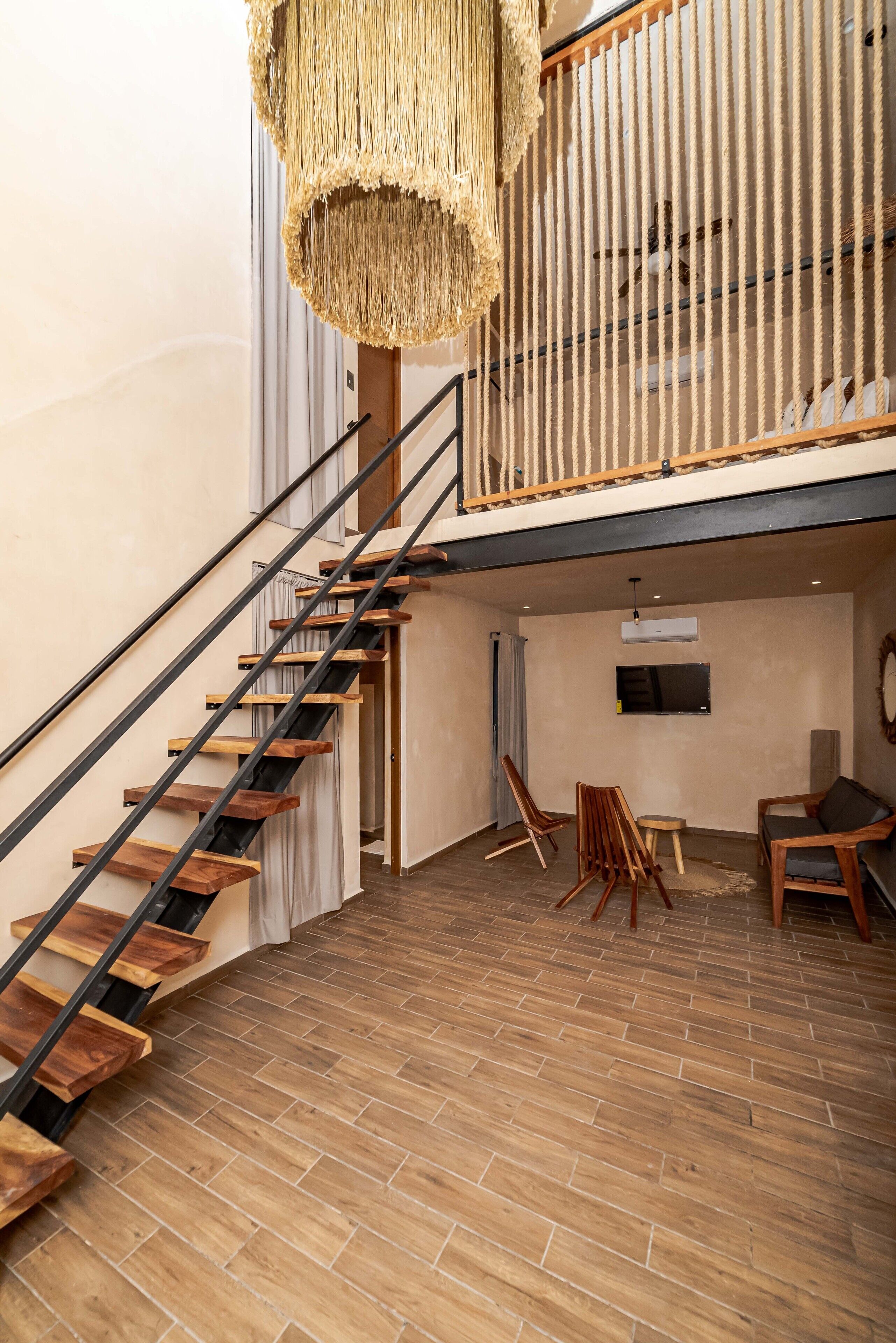 A spacious room with a wooden staircase, a hanging light fixture, and a flat-screen TV mounted on the wall.