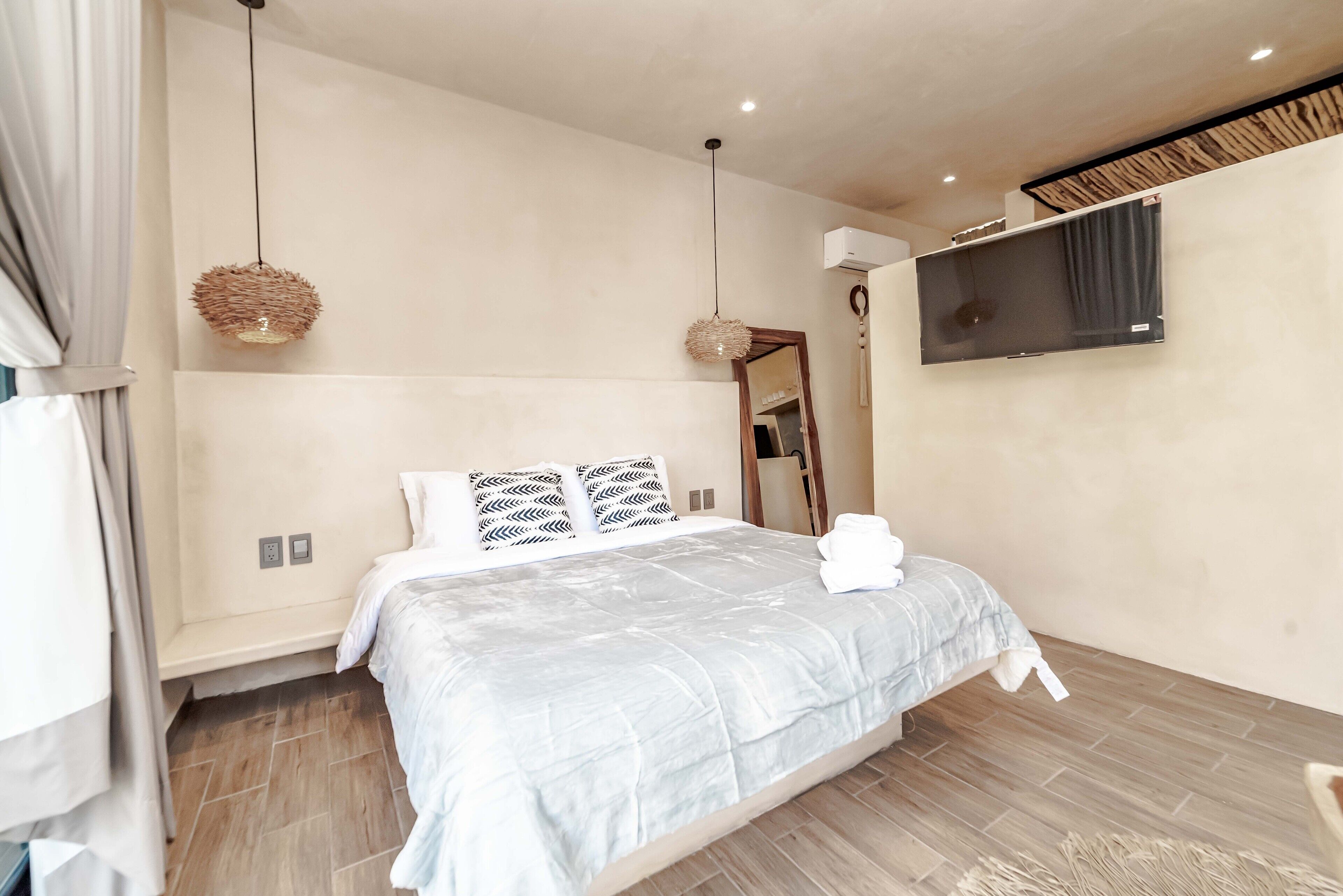 A modern bedroom with a bed, two hanging lights, a flat-screen TV, and a mirror.