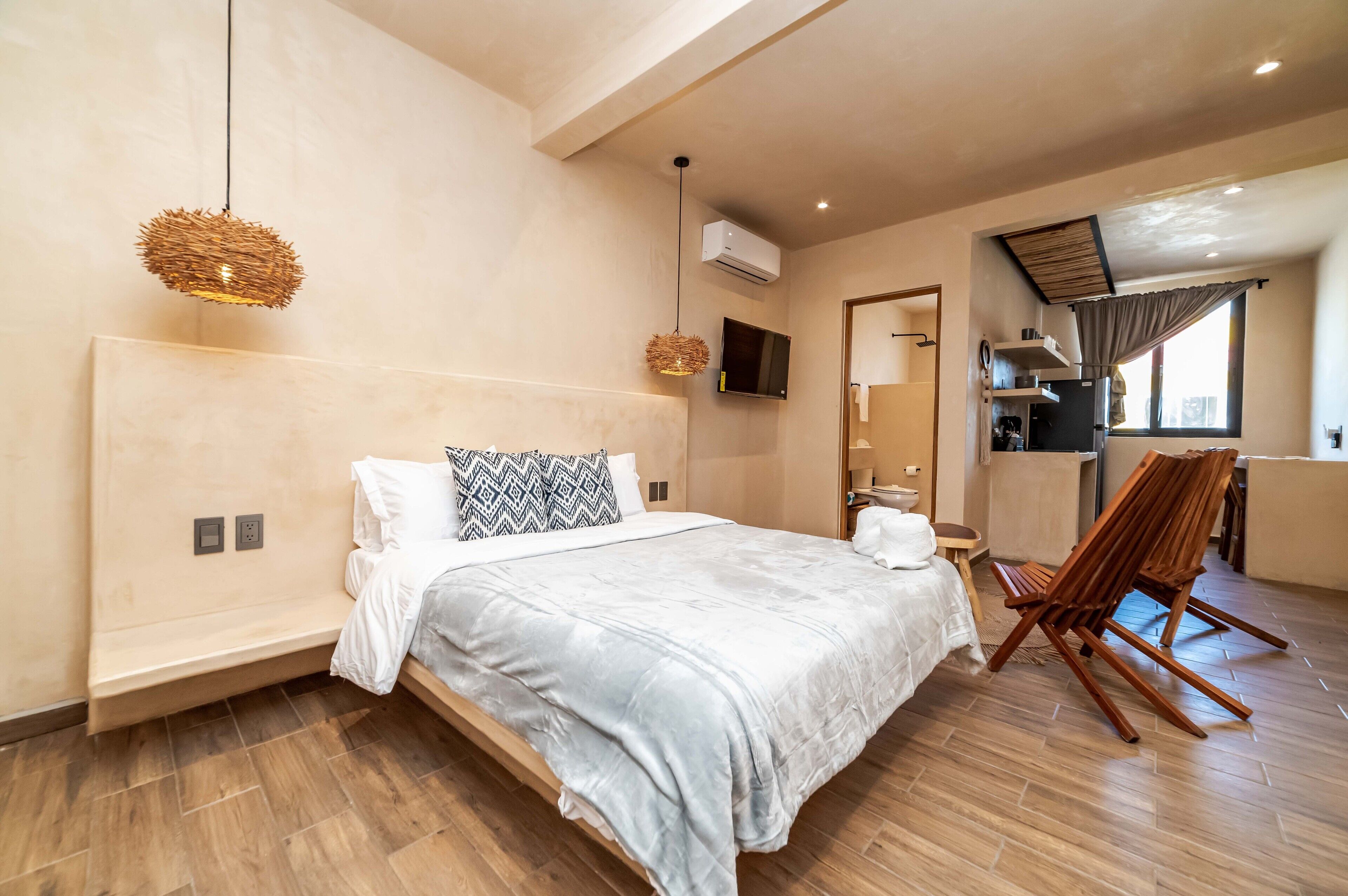 A modern bedroom with a large bed, a TV mounted on the wall, and a wooden chair.