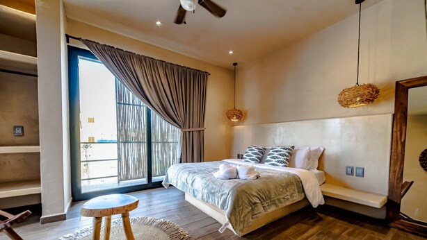 A modern bedroom with a large bed, a wooden floor, a round wooden stool, and a woven rug. - The Teodoro (Tulum)