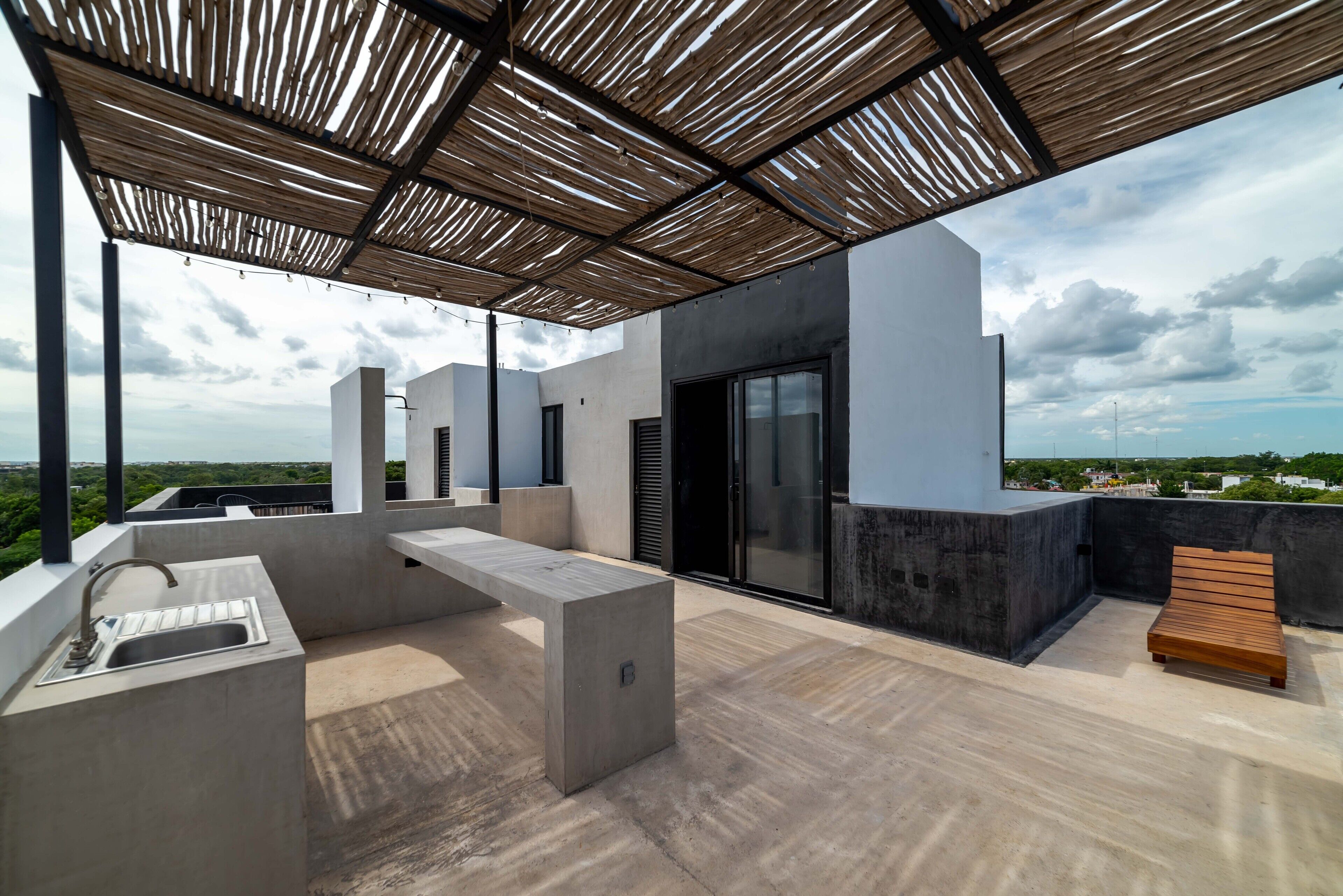A rooftop terrace with a concrete bench, a wooden bench, a sink, and a view of the city.